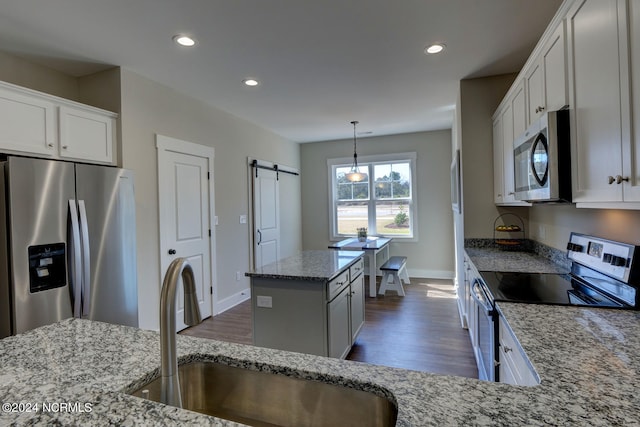 kitchen featuring sink, light stone counters, white cabinetry, stainless steel appliances, and a barn door