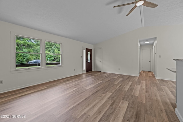 unfurnished living room featuring light hardwood / wood-style flooring, vaulted ceiling, ceiling fan, and a textured ceiling