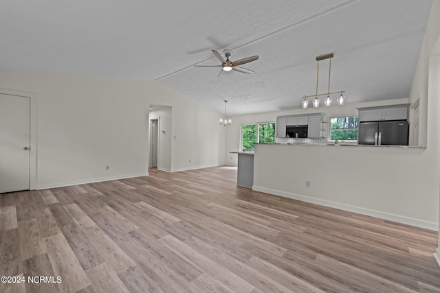 unfurnished living room with ceiling fan with notable chandelier, light wood-type flooring, vaulted ceiling, and a textured ceiling