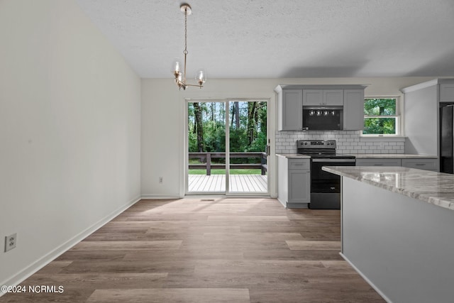 kitchen with gray cabinetry, light hardwood / wood-style flooring, backsplash, range with electric cooktop, and an inviting chandelier