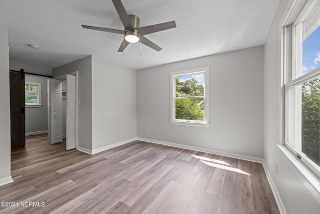 empty room with ceiling fan, light wood-type flooring, a barn door, and a healthy amount of sunlight