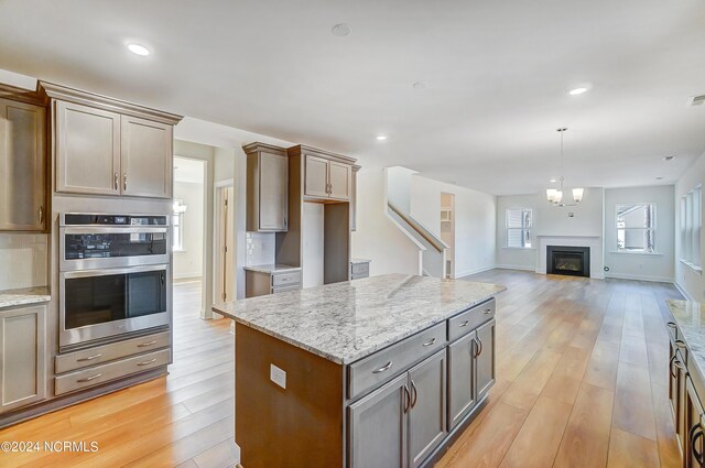 kitchen with light stone countertops, light hardwood / wood-style floors, a center island, and stainless steel double oven