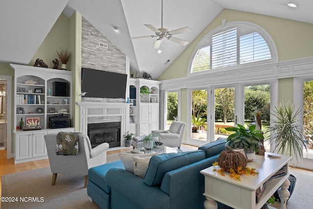 living room featuring a fireplace, light wood-type flooring, built in shelves, high vaulted ceiling, and ceiling fan