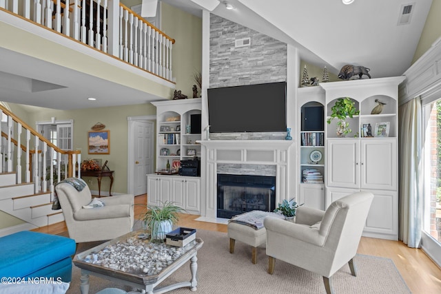 living room featuring high vaulted ceiling, built in shelves, a high end fireplace, and light wood-type flooring