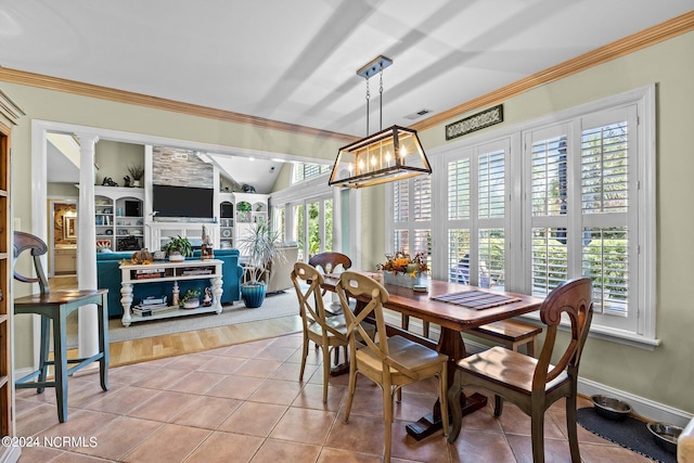 tiled dining space with decorative columns, built in shelves, crown molding, and an inviting chandelier