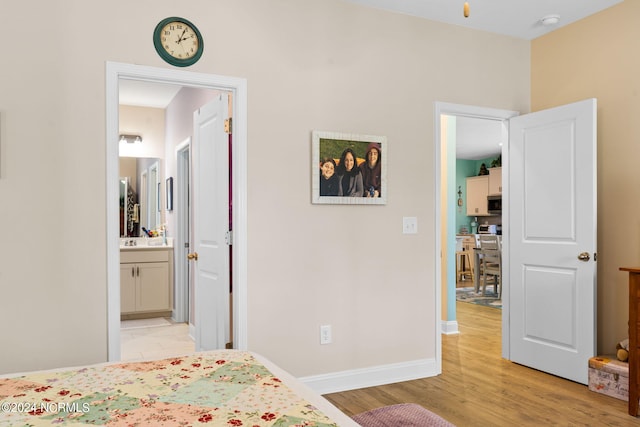 bedroom with light wood-type flooring, baseboards, and ensuite bathroom