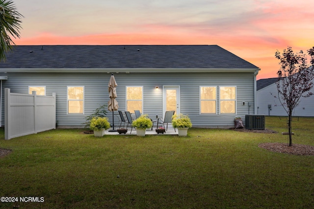 back of house with central air condition unit, a shingled roof, fence, a yard, and a patio area