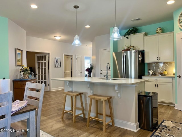 kitchen with a center island with sink, pendant lighting, light countertops, and freestanding refrigerator