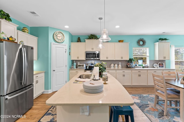 kitchen featuring a center island with sink, decorative light fixtures, stainless steel appliances, light countertops, and white cabinetry