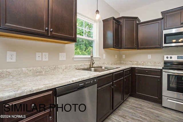 kitchen with dark brown cabinetry, pendant lighting, sink, appliances with stainless steel finishes, and light hardwood / wood-style floors