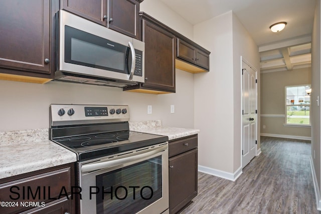 kitchen with appliances with stainless steel finishes, coffered ceiling, beamed ceiling, dark brown cabinets, and hardwood / wood-style flooring