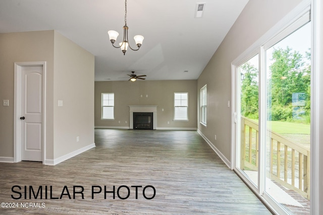 unfurnished living room featuring ceiling fan with notable chandelier, hardwood / wood-style flooring, and plenty of natural light