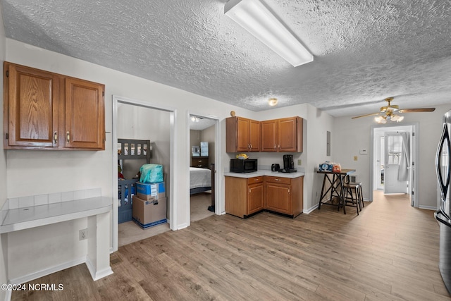 kitchen featuring a textured ceiling, stainless steel fridge, light hardwood / wood-style floors, and ceiling fan