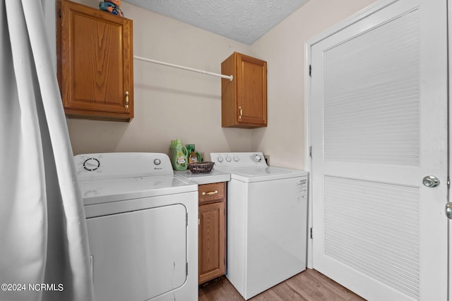 laundry area featuring cabinets, separate washer and dryer, a textured ceiling, and light wood-type flooring