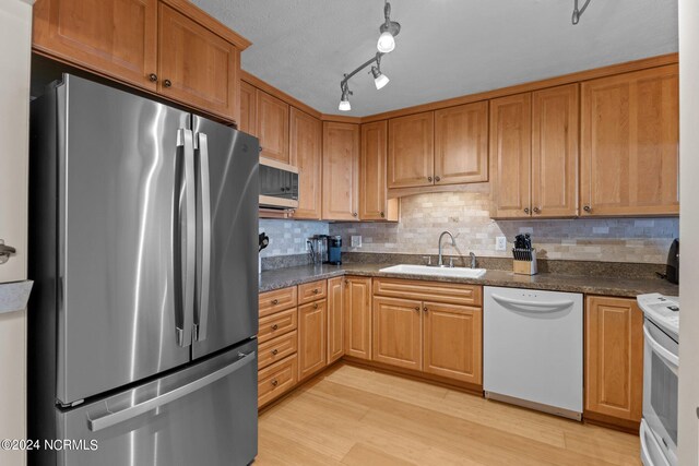 kitchen with appliances with stainless steel finishes, decorative backsplash, light hardwood / wood-style floors, dark stone countertops, and sink