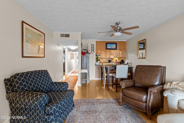 living room featuring ceiling fan, a textured ceiling, crown molding, and light hardwood / wood-style floors