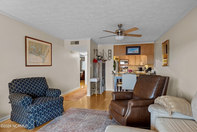 living room featuring a textured ceiling, light hardwood / wood-style floors, ceiling fan, and crown molding