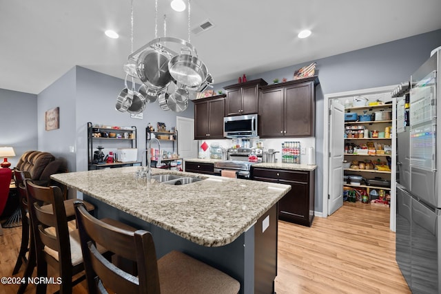 kitchen featuring an island with sink, sink, stainless steel appliances, dark brown cabinets, and light hardwood / wood-style flooring