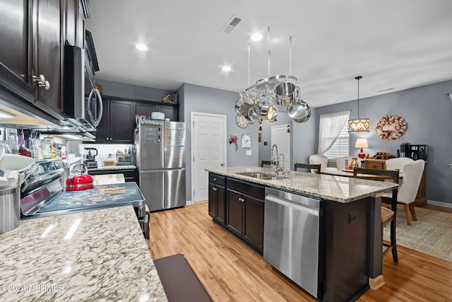 kitchen with appliances with stainless steel finishes, sink, hanging light fixtures, a kitchen island with sink, and light stone counters