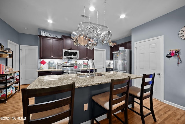 kitchen featuring sink, appliances with stainless steel finishes, dark brown cabinets, an island with sink, and a kitchen bar