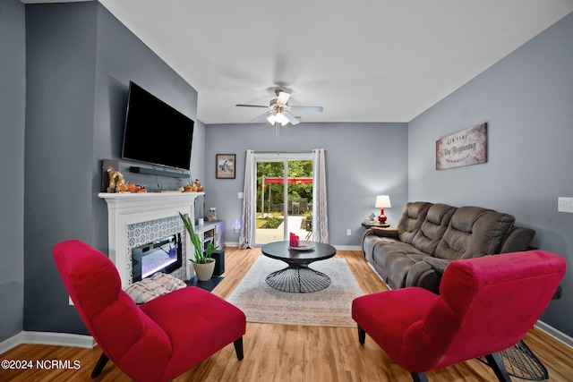 living room with a tile fireplace, wood-type flooring, and ceiling fan