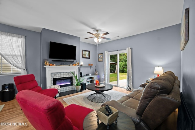 living room featuring hardwood / wood-style flooring, ceiling fan, and a tiled fireplace