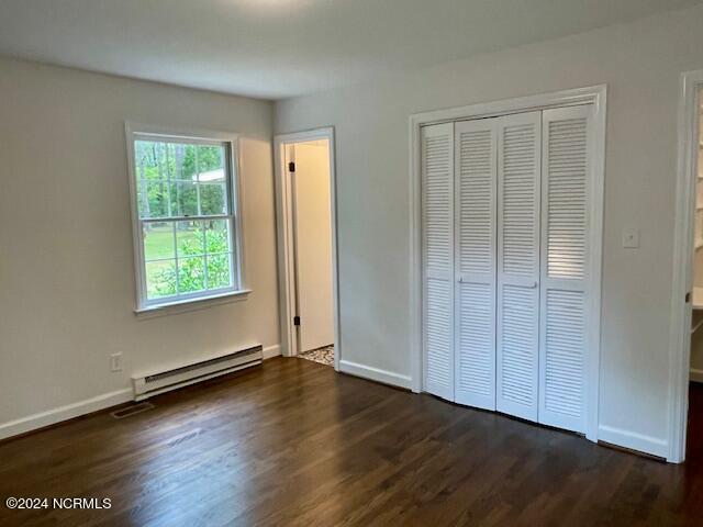 unfurnished bedroom with a baseboard heating unit, dark wood-type flooring, baseboards, and a closet