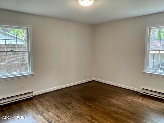 empty room featuring baseboard heating, visible vents, baseboards, and wood finished floors