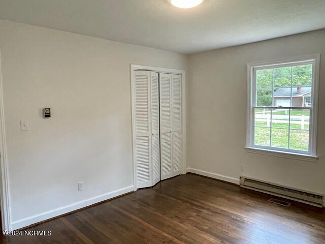 unfurnished bedroom with a closet, baseboards, baseboard heating, and dark wood-type flooring