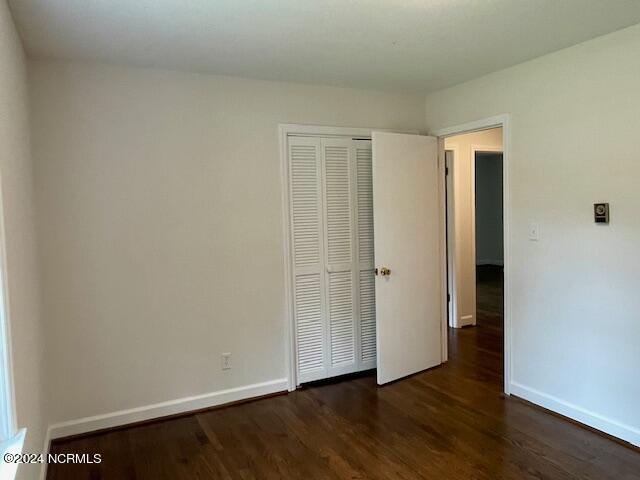 unfurnished bedroom featuring dark wood finished floors, baseboards, and a closet