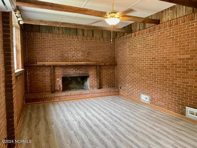 unfurnished living room with wood-type flooring, ceiling fan, brick wall, and a brick fireplace