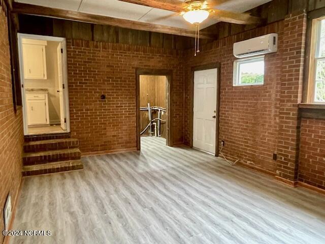 unfurnished room featuring brick wall, beam ceiling, ceiling fan, light hardwood / wood-style flooring, and a wall mounted AC