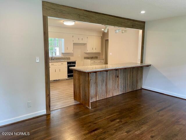 kitchen with oven, dark wood-type flooring, a peninsula, white cabinetry, and a sink