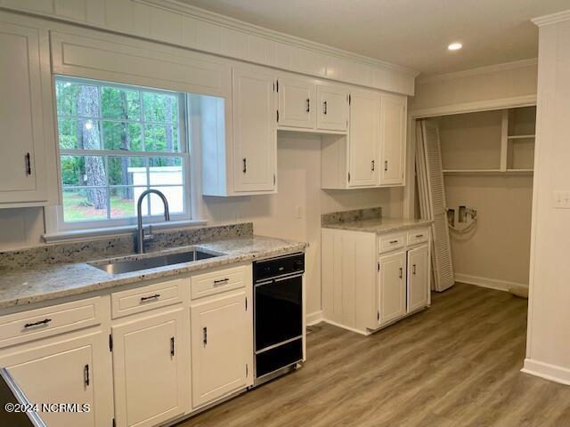 kitchen featuring white cabinets, light stone countertops, wood-type flooring, crown molding, and sink