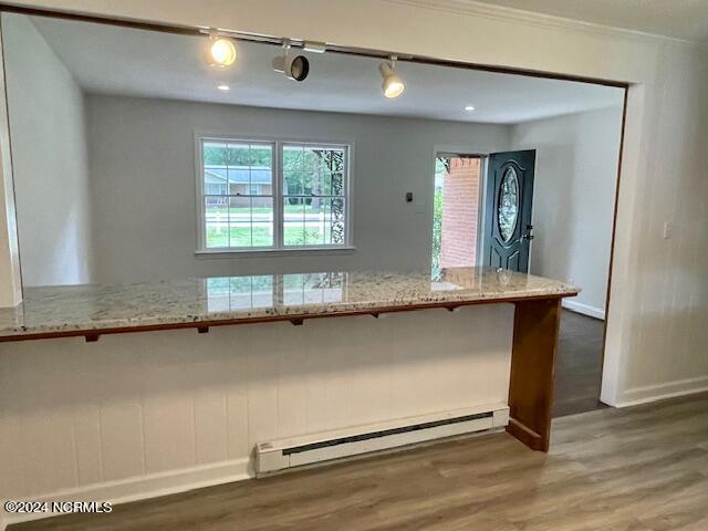 kitchen with a kitchen breakfast bar, wood finished floors, baseboards, a baseboard radiator, and light stone countertops