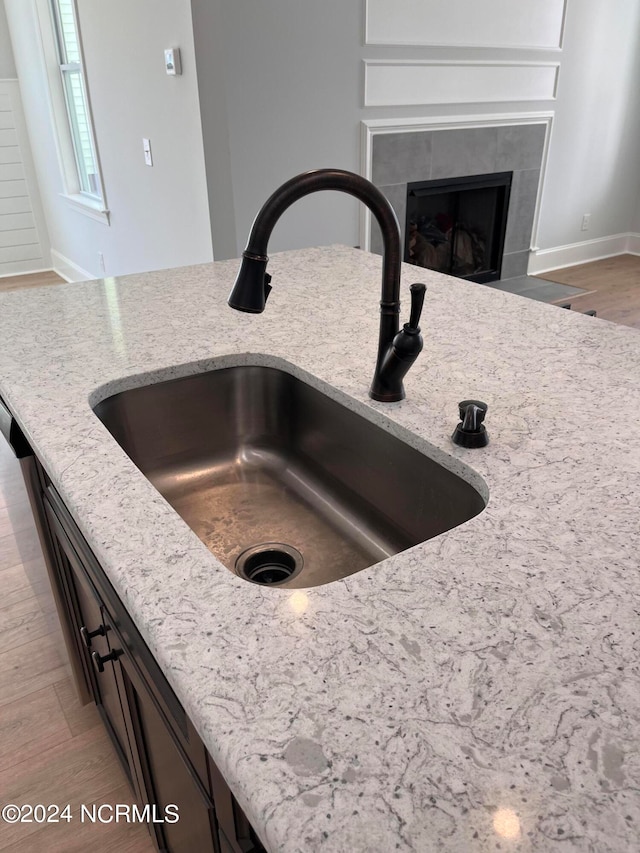 details featuring light stone counters, light wood-type flooring, sink, and a tile fireplace