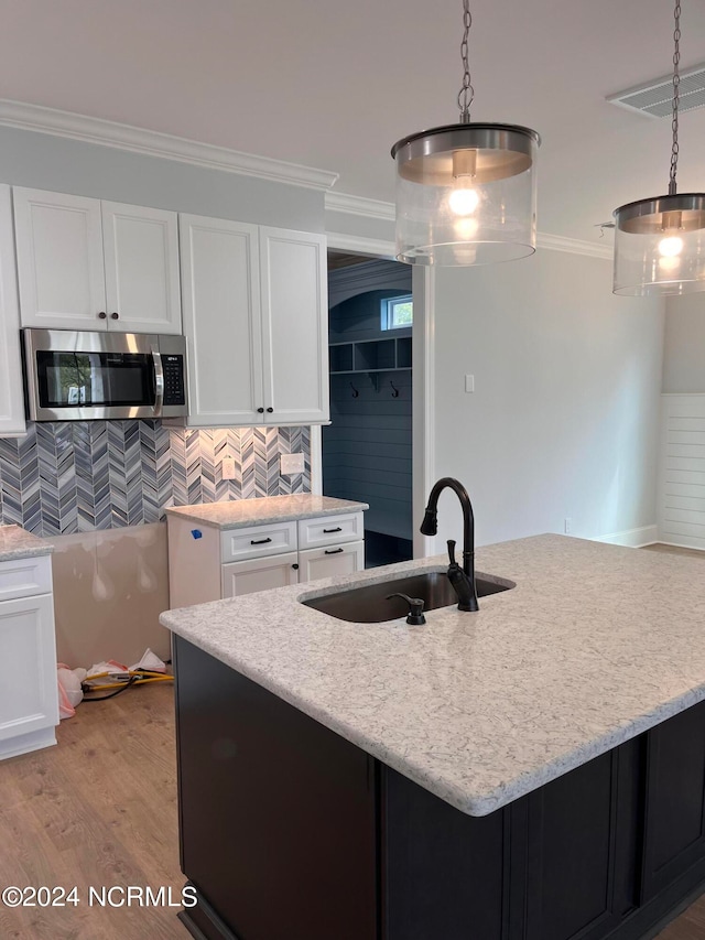 kitchen featuring light wood-type flooring, decorative light fixtures, a center island with sink, ornamental molding, and sink