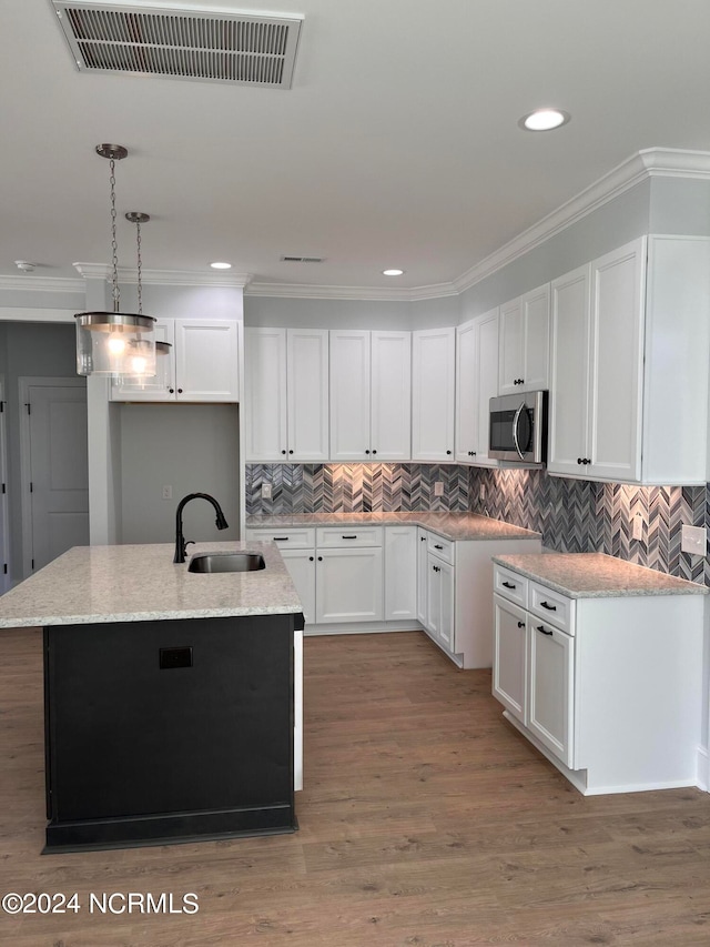 kitchen featuring white cabinets, sink, a center island with sink, decorative light fixtures, and hardwood / wood-style flooring