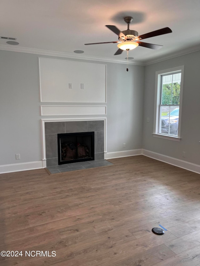 unfurnished living room featuring wood-type flooring, ornamental molding, a tiled fireplace, and ceiling fan