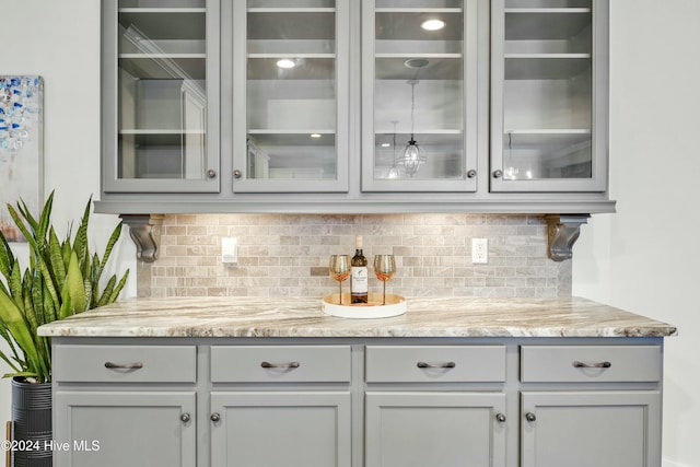 bar with backsplash, light stone counters, and gray cabinetry