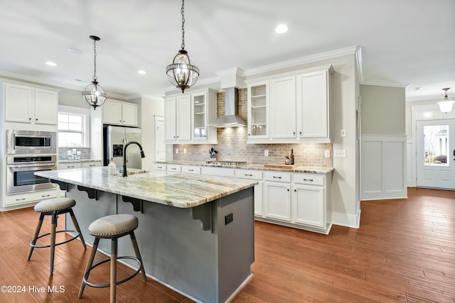 kitchen featuring stainless steel appliances, white cabinetry, a kitchen island with sink, and wall chimney range hood