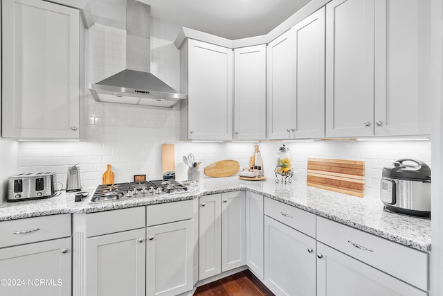 kitchen featuring wall chimney exhaust hood, stainless steel gas stovetop, white cabinetry, and tasteful backsplash