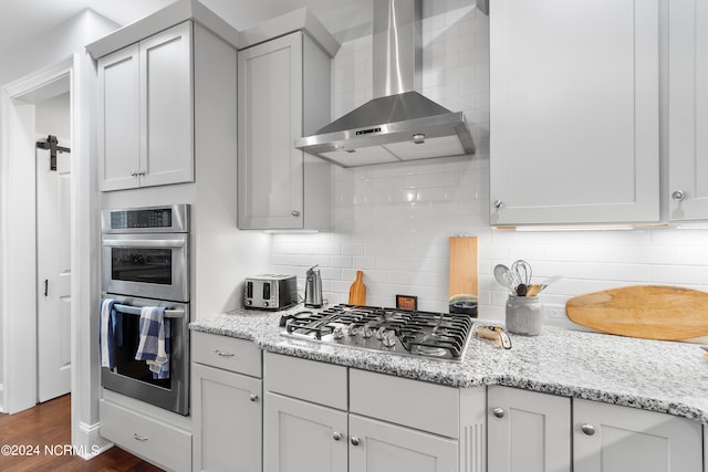 kitchen with backsplash, appliances with stainless steel finishes, dark wood-type flooring, wall chimney exhaust hood, and light stone counters