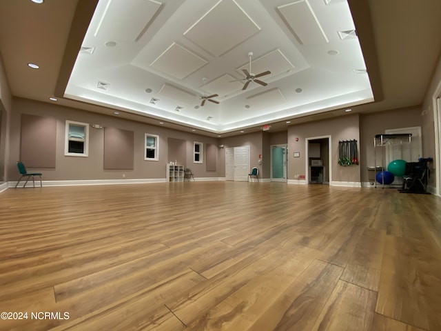 exercise room featuring ceiling fan, light wood-type flooring, and a raised ceiling