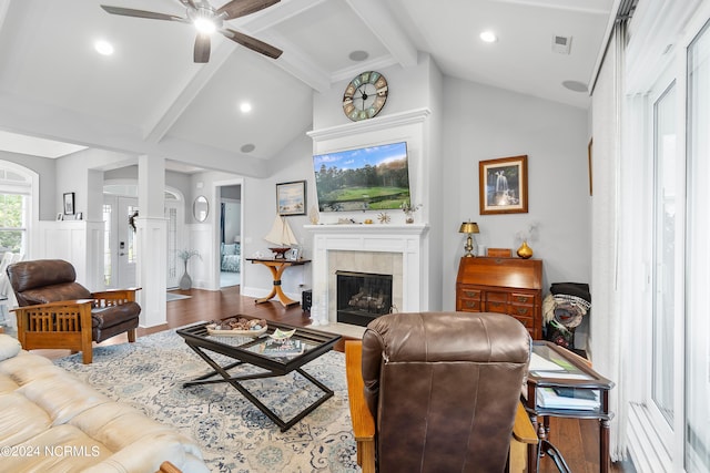 living room featuring ceiling fan, hardwood / wood-style flooring, vaulted ceiling with beams, and a tile fireplace