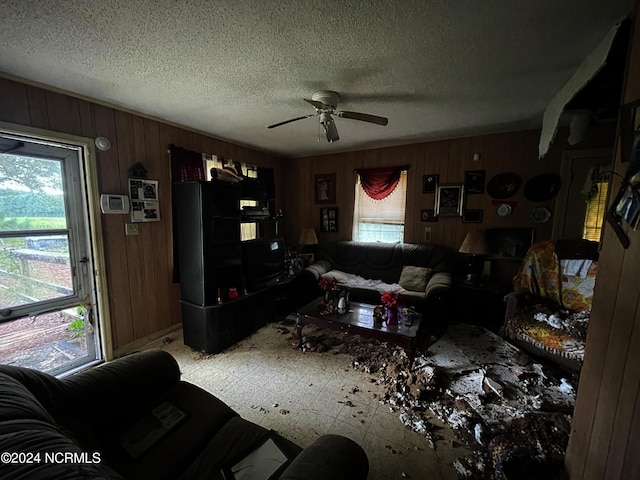 living room featuring ceiling fan, a textured ceiling, wood walls, and a healthy amount of sunlight