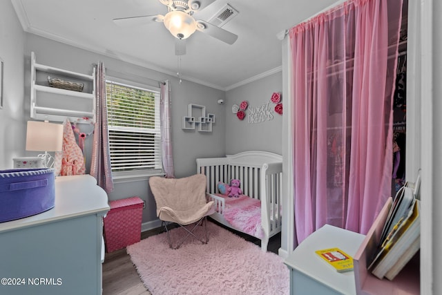 bedroom with ceiling fan, a crib, ornamental molding, and wood-type flooring