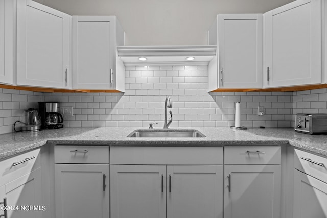 kitchen with light stone countertops, backsplash, sink, and white cabinets