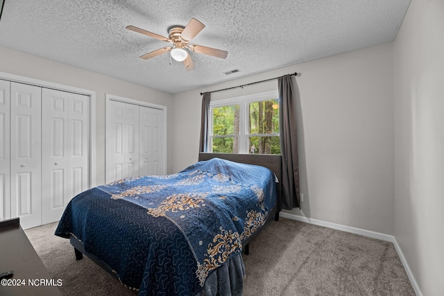 carpeted bedroom with a textured ceiling, two closets, and ceiling fan