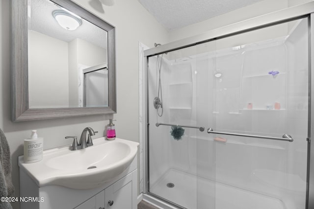 bathroom with a textured ceiling, vanity, and a shower with shower door